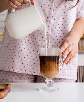 Alternative coffee brewing. young woman in lovely pajamas making coffee at home kitchen adding milk