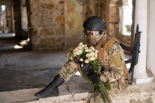 Caucasian woman in military uniform holding a machine gun and a bouquet of white roses