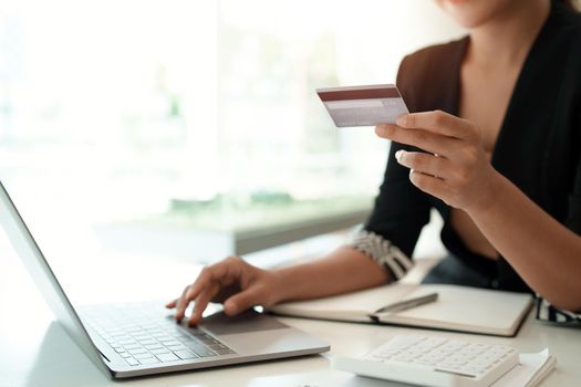 Asian girl making online payment using laptop and credit card for shopping at home.