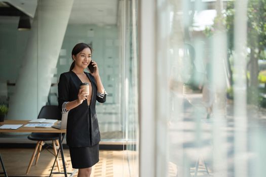 Asian business woman making a phone call and smiling at modern office.