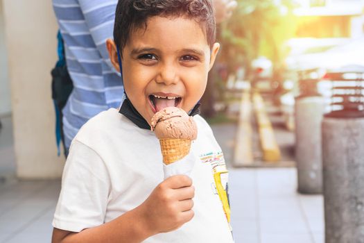Latin boy with mischievous face enjoying an ice cream during the summer break in a shopping center hand in hand with his mother