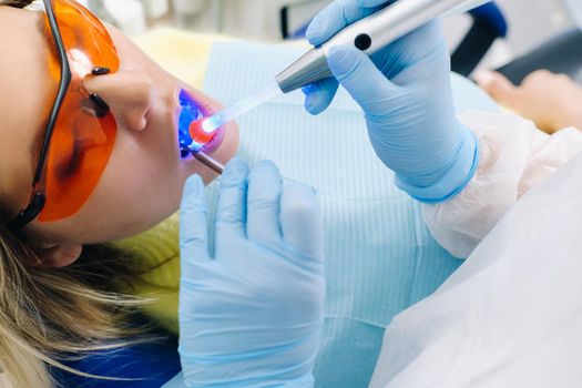 A female patient in dental glasses treats teeth at the dentist with ultraviolet light. dental fillings.