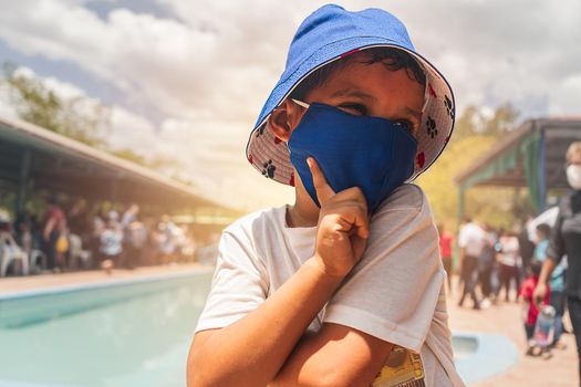 Latin boy enjoying summer in a pool very happy dressed in comfortable clothes and a bucket hat and mask