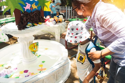 Latin mother and son participating in a summer fair game called fishing. Participants must catch a toy fish and receive a prize.