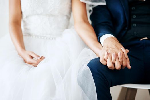 Studio shot of two unrecognizable young newlyweds holding hands against a gray background.