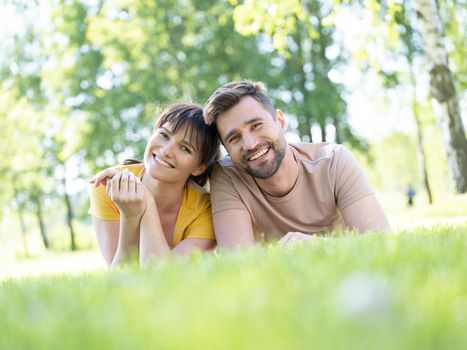 Fun and love concept with mid adult couple lying down in grass looking to camera and smiling