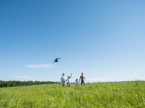 Family of parents and children running through field letting kite fly