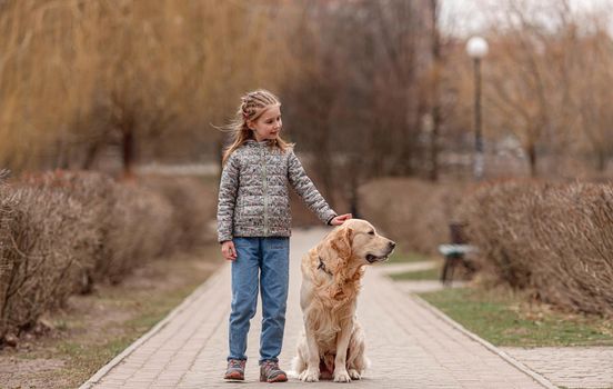 Preteen girl and golden retriever dog looking back together in the park