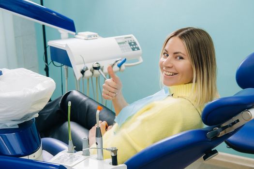 Beautiful girl patient shows the class with her hand while sitting in the Dentist's chair.