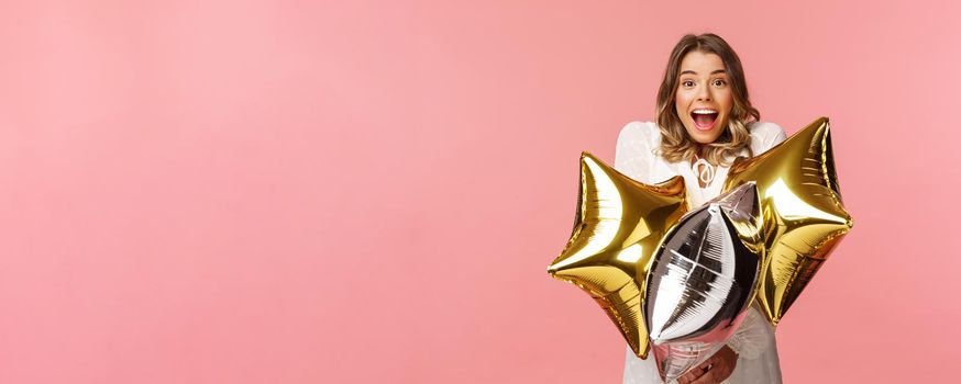 Holidays, celebration and women concept. Happy charming and surprised girl being congratulated with birthday, holding star-shaped balloons and smiling joyfully camera, pink background.