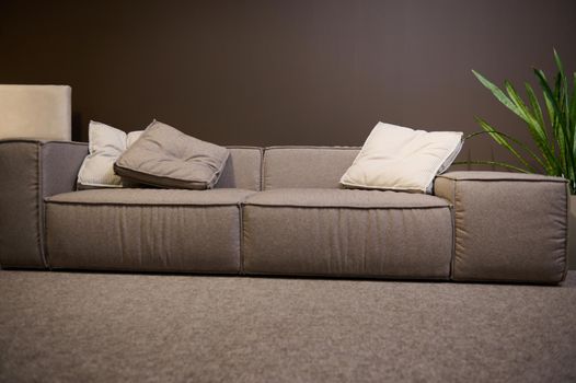 Front view of a large comfortable sofa made of high quality fabrics and soft cushions, on display for sale in the showroom of a furniture store. Home interior design, living room decoration