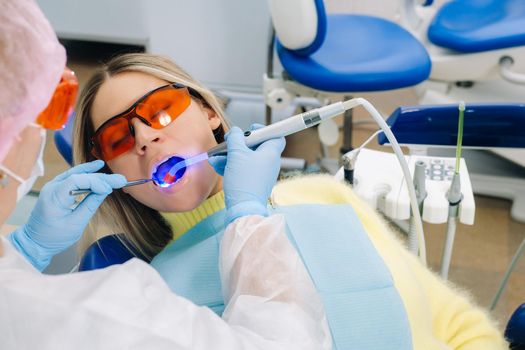 A female patient in dental glasses treats teeth at the dentist with ultraviolet light. dental fillings.