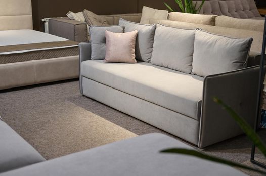 Exposition of upholstered modern comfortable light gray settee with pink cushions near a stand with swatches and fabric samples of different textures and qualities. Furniture store showroom