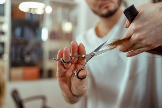 Hairdresser holding scissors in his hands and cutting client hair. Beauty salon services concept