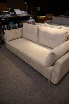 Exhibition of soft furnishing. Stylish comfortable beige settee with cpillows near a stand with fabric samples for upholstery in the showroom of a furniture store. Home design and decoration concept