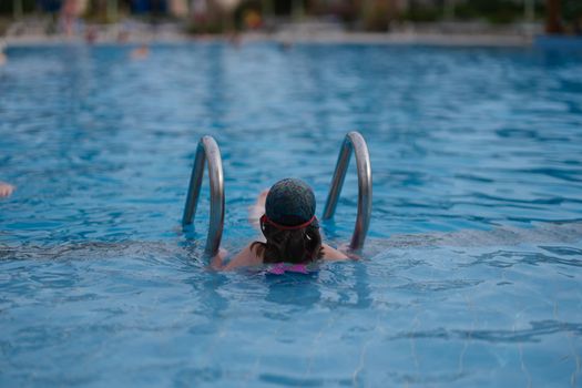 Little girl swimming in pool on vacation back view. Swimming lessons for children concept
