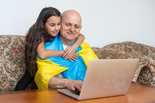 Grandfather and granddaughter with laptop and flag of Ukraine.