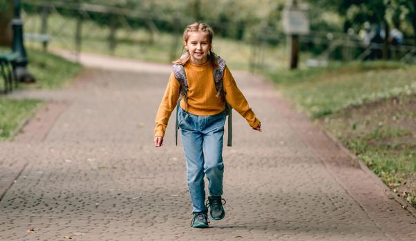 Pretty school girl with backpack running in the park after lessons. Sweet child kid at autumn outdoors