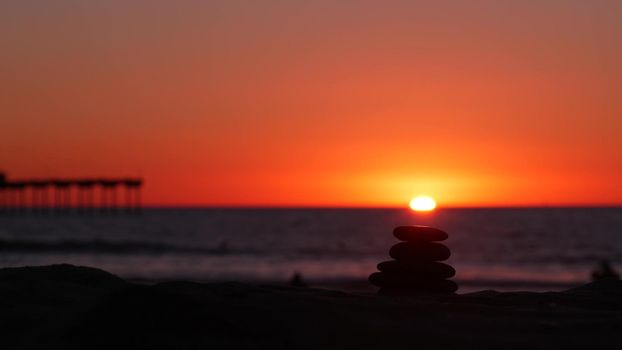 Stack of pebble stones, sandy ocean beach, sunset sky. Rock balancing in sun light, sea water waves. Stones staking in pyramid pile. Zen meditation and harmony in balance. Seamless looped cinemagraph.
