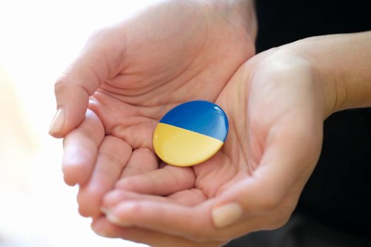 Female hands holding badge with flag of Ukraine closeup. Support of Ukrainian people during war concept