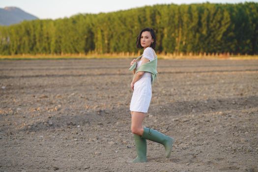 Pretty young Asian woman, walking in the countryside, wearing a white dress and green wellies.