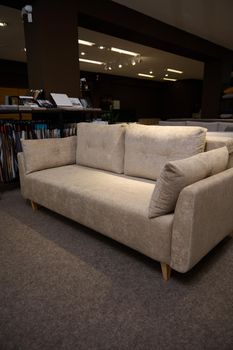 Stylish comfortable settee with pillows near a stand with fabric samples for upholstery in the showroom of furniture store. Living room furnishing with stylish modern comfortable upholstered furniture