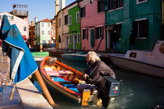 Burano, Italy - January, 06: Italian elderly on his boat navigating in the Burano canal on January 06, 2022