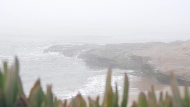 Foggy sea landscape, waves crashing on ocean beach in haze, misty weather. Calm tranquil moody atmosphere, grey seascape, gloomy dramatic California coast, stormy water. Seamless looped cinemagraph.
