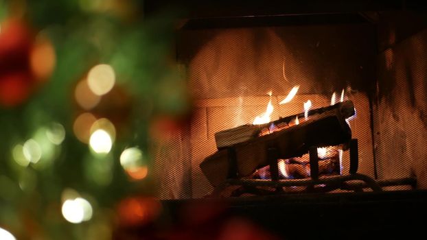 Christmas tree lights by fire in fireplace, New Year or Xmas decoration of pine or fir with red balls. Fireside on winter christmastime holiday. Cozy place by firewood. Seamless looped cinemagraph.