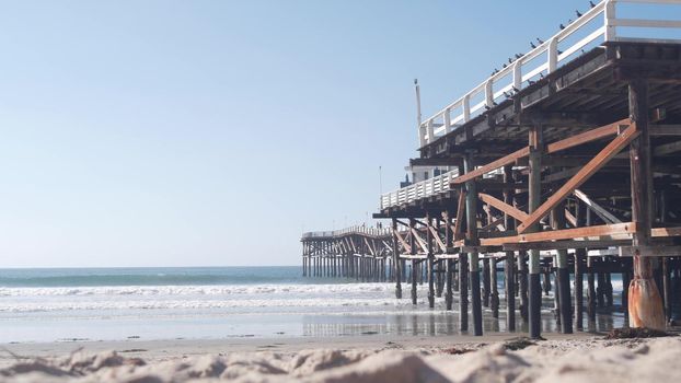Below wooden Crystal pier on piles, ocean beach water waves, California USA. Summer vacations on Mission beach, San Diego shore. Under waterfront promenade on sea coast. Seamless looped cinemagraph.