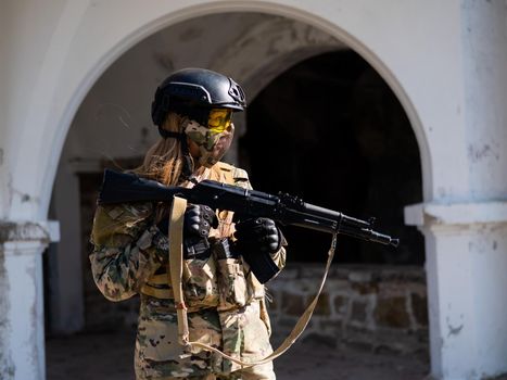 Caucasian woman in a protective suit with a machine gun. FA female soldier in a camouflage uniform holds a weapon