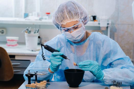 A dental technician in protective clothing is working on a prosthetic tooth in his laboratory.