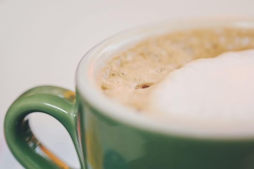 Coffee in green cappuccino ceramic cup with frothy foam, latte capuccino mug closeup. Hot coffee latte in jade color porcelain cup on table in cafe close up. Selective focus