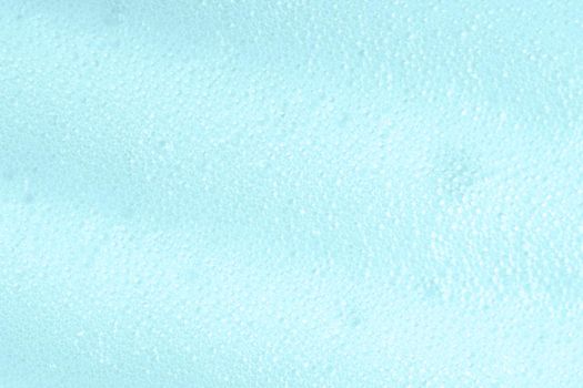 Blue soapy surface closeup. Foamy cleansing skin care product texture from soap, shaving foam or cleanser. Foam macro background with bubbles. Laundry spume