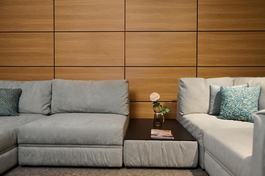 Modern stylish comfy soft upholstered gray sofa with green pastel pillows and a journal table with a rose in the vase in the showroom of a furniture store