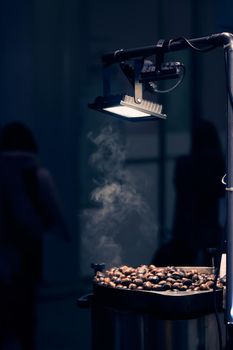 Grillled chestnuts in the night city under street lamp. Fried chestnut vendor, street food. Milan, Italy - December 25, 2019