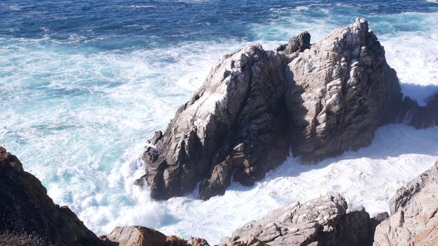 Rocky craggy ocean beach. Big waves crashing on bare cliff, blue water splashing, sea foam. Power of nature near Big Sur, 17-mile drive. Dramatic seascape. Point Lobos, Monterey, California coast, USA
