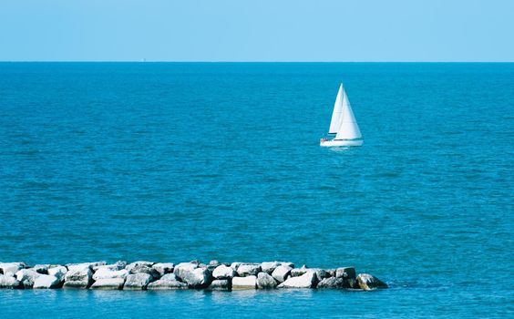 Sloop rigged yacht sailing in a Mediterranean sea on a clear sunny day. Sailboat, yawl sailing in an open sea. Coast of Rimini, Italy. Sport, cruise, recreation, leisure activity.