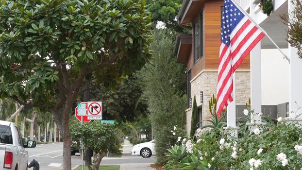 American flag waving on flagpole, suburban house facade, San Diego city street in residential district. Private property, typical building with patriotic symbol. Single-family home architecture in USA
