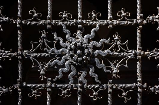 Ornate curly metal grid on religious building in Milan on sunny day. Exterior part of antique church. Vintage picturesque window in european city. European architecture