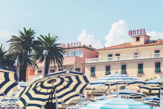 Beach umbrellas with view on coastal hotel Corallo in italian coastline Finalmarina. Summer beach. Finale ligure - August 23, 2020