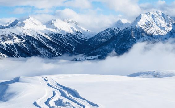 Mountain ski resort. Snowcat trail on snow slope. Snowy mountains. Ski resort landscape on clear sunny day. Panoramic view of mountains near Brianson, Serre Chevalier resort. Winter vacation..