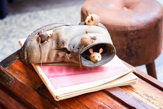 Close-up mice and brown shoes on wooden chest. Mouse sleeping in old torn brown shoe. Figurines in street european market