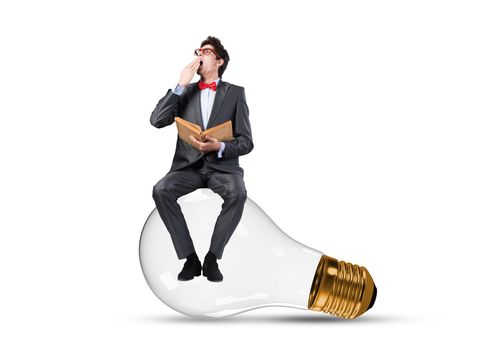 Young businessman sits on an electric light bulb. holds a book in his hands