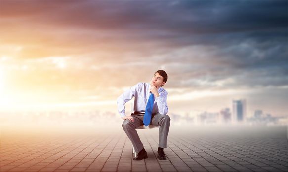 young businessman sits on an office chair, thoughtful and looking up