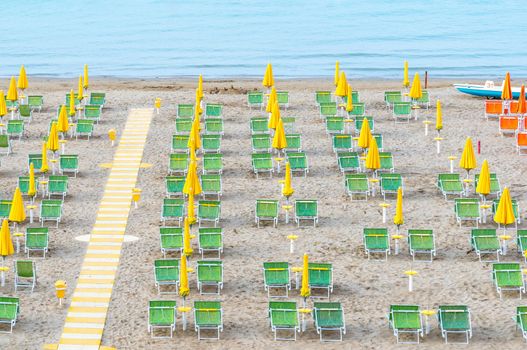 Lounge chairs on sand beach in Italy. Beach lounge area with yellow umbrellas and green sunbeds on italian coastline. End of the season. .