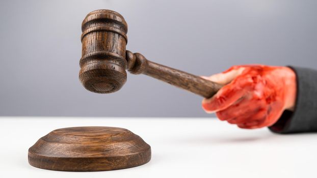 Female judge with bloody hands beats the gavel on a white background