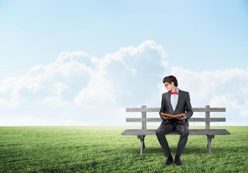 young student with a book. sits on a wooden bench