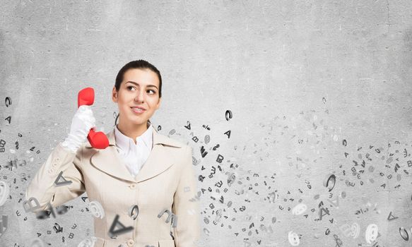 Smiling young woman holding retro red phone and flying various letters. Call center operator in business suit with phone. Hotline telemarketing and consultation. Business assistance service.