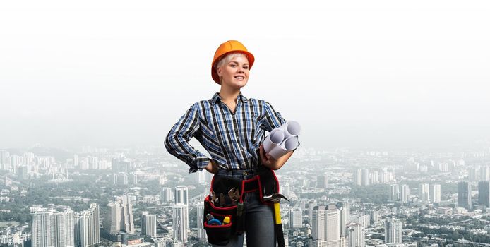 Attractive female engineer in hardhat standing with technical blueprints. Portrait of young architect in checkered blue shirt on background of cityscape. Architecture and construction company.